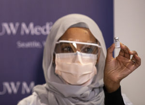 Black healthcare worker in head covering and mask holds up vaccine vial